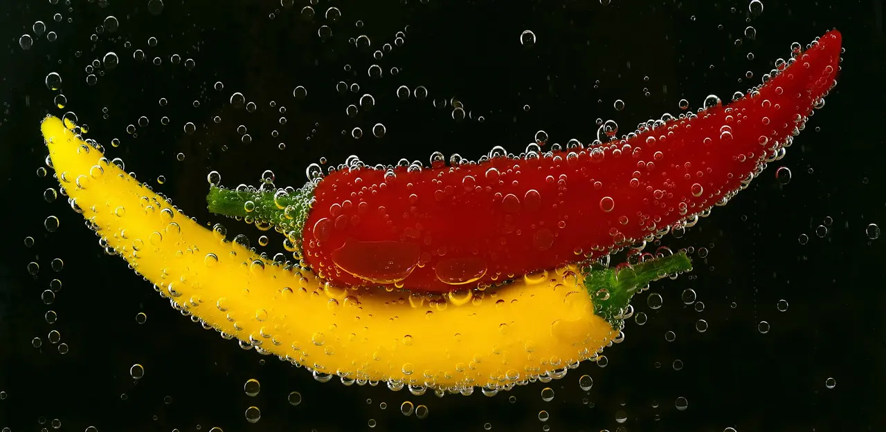 A red and a yellow chilli pepper under water, covered in bubbles