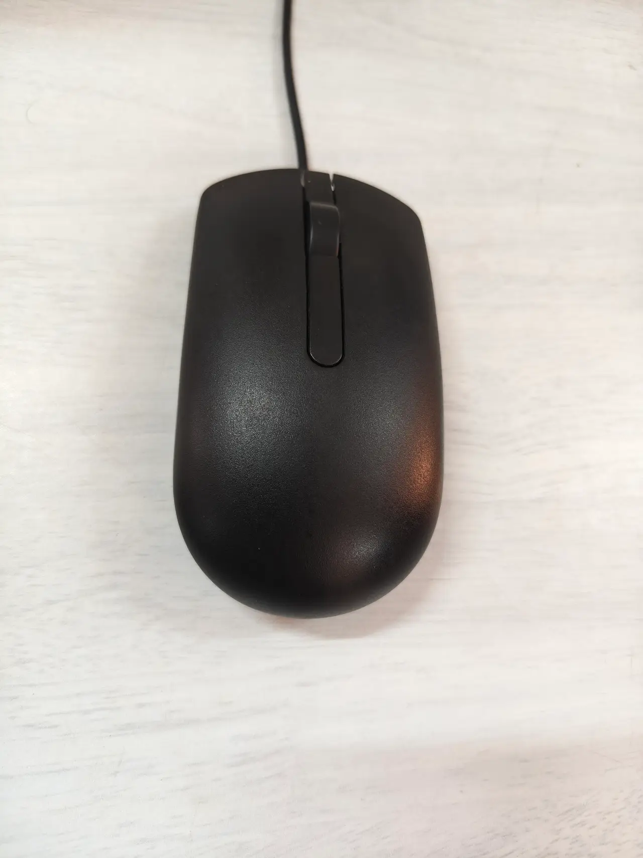 A black wired computer mouse seen from above on a pale surface