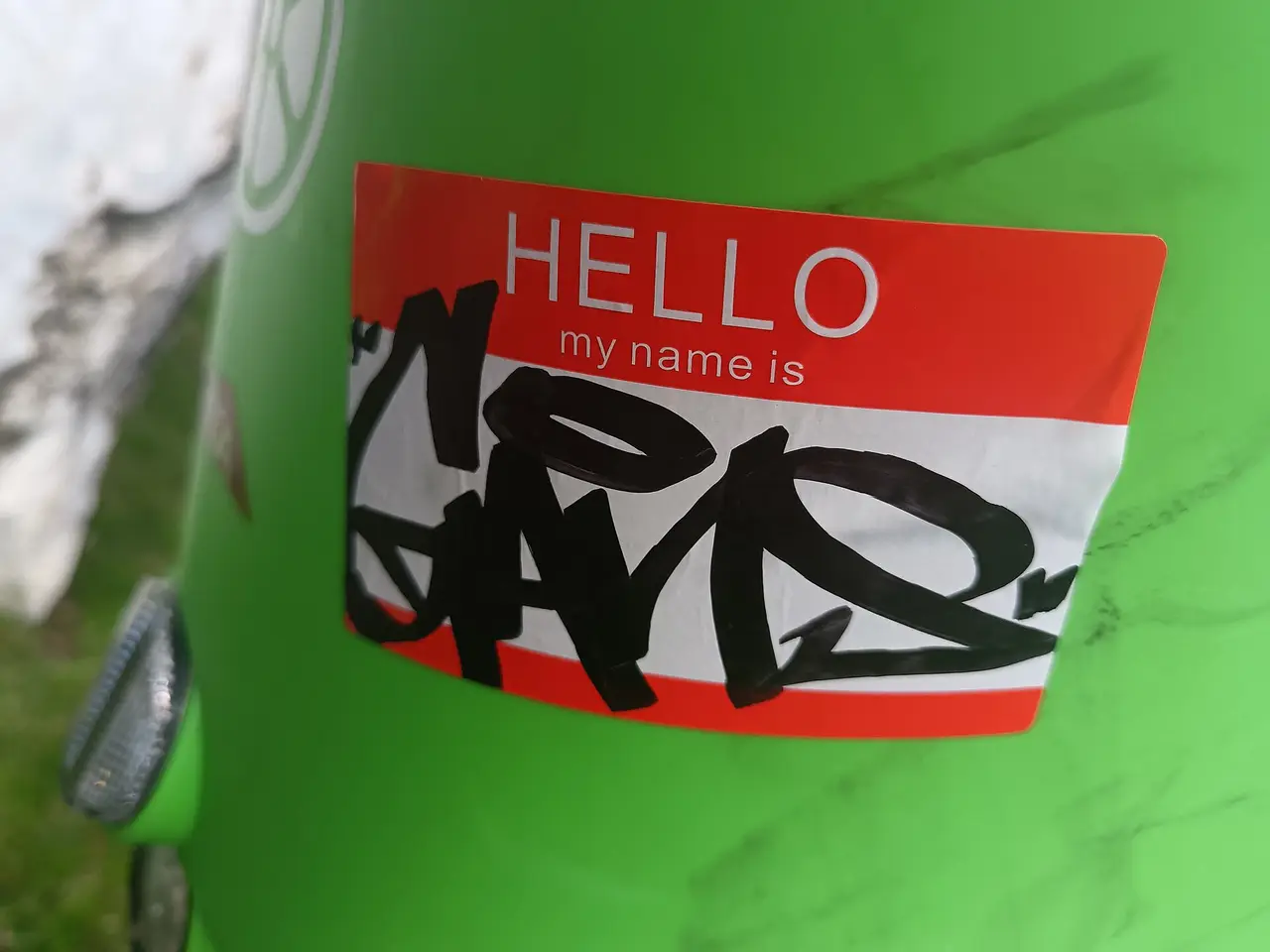Red name tag sticker with a black graffiti tag on a green bin