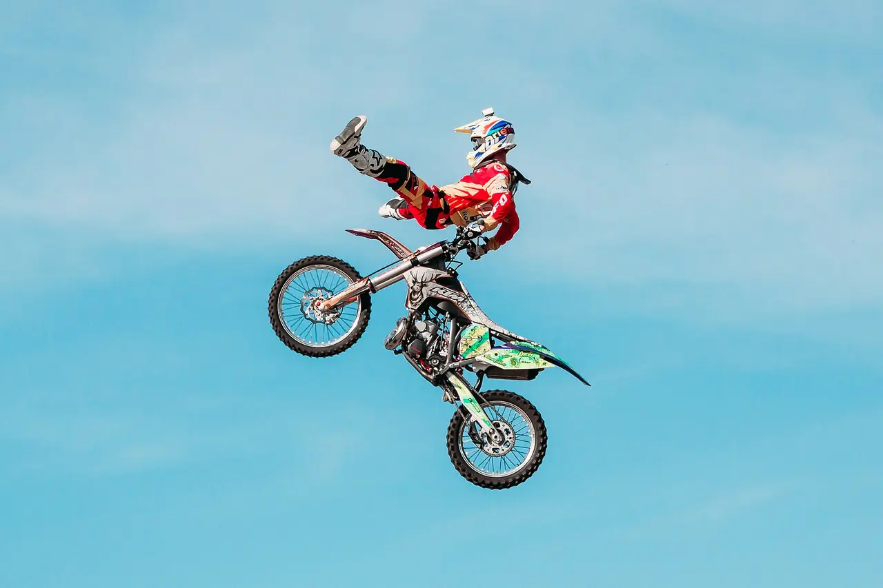 Motocross rider in a red jersey airborne above a green bike