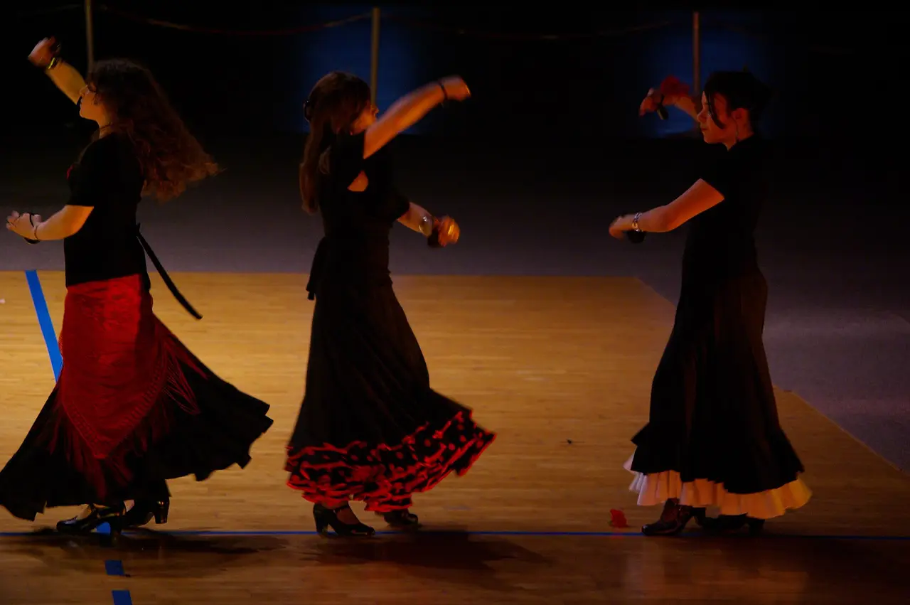 Three dancers in long black skirts on a polished stage floor