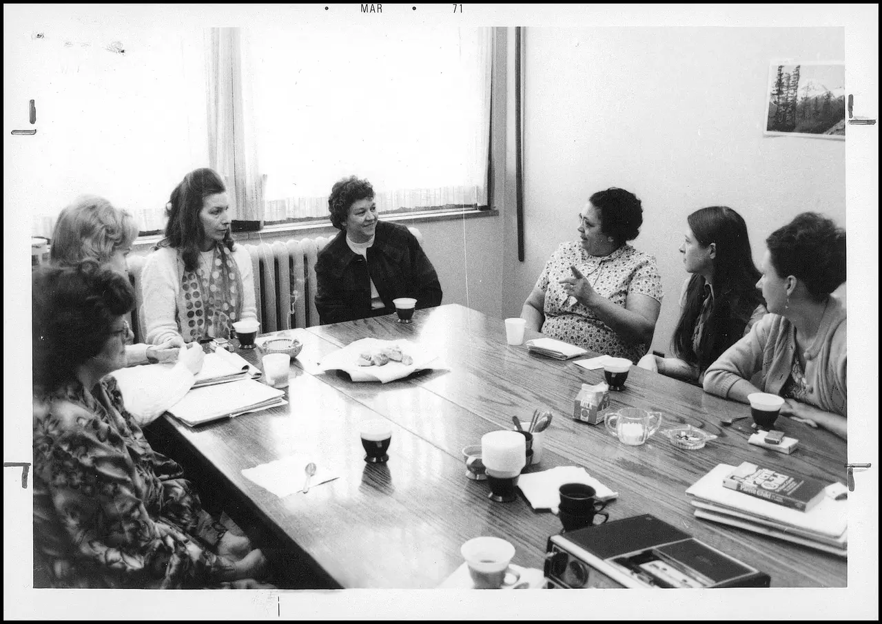 Women seated around a table with coffee cups in a black and white photo