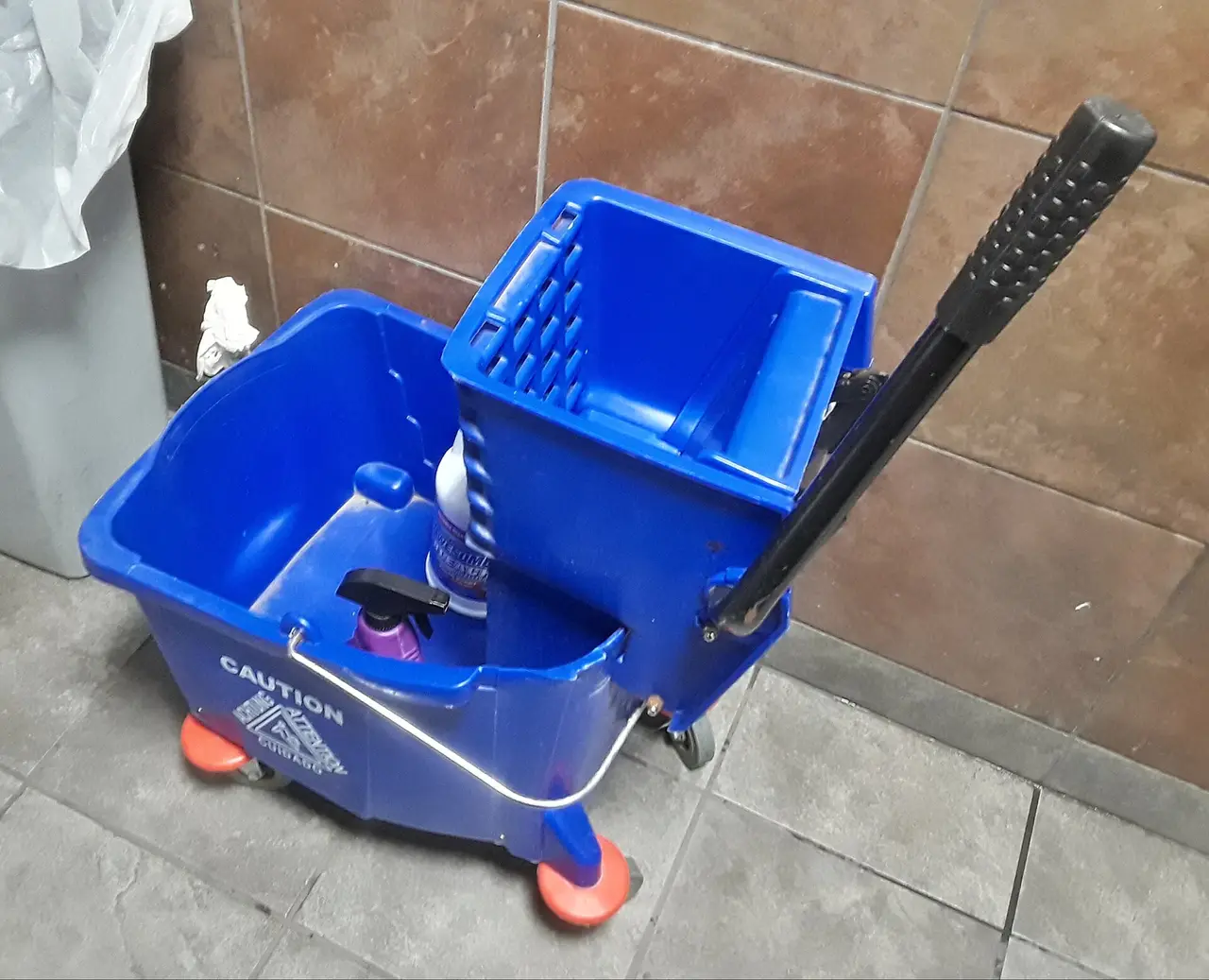 Blue mop bucket with wringer beside a tiled wall