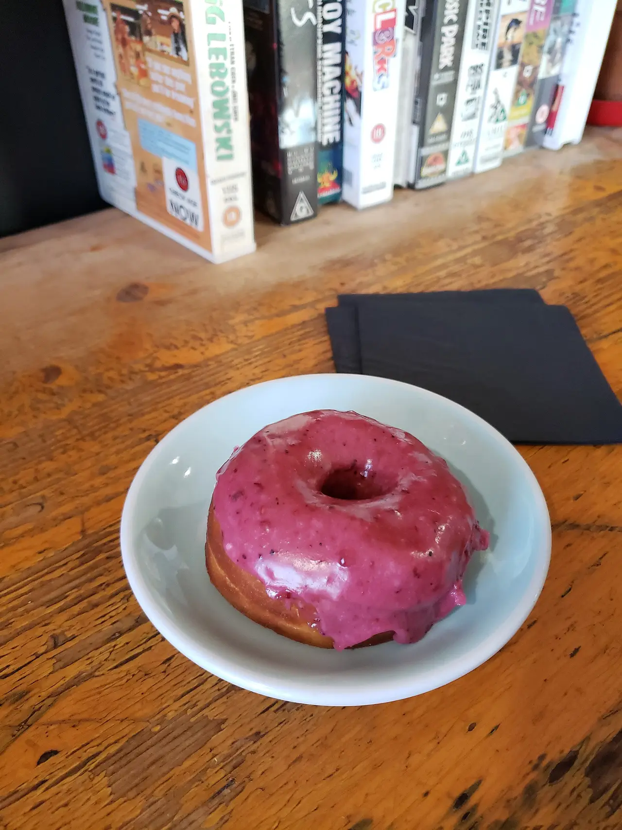 Donut with pink icing on a white plate on a wooden table