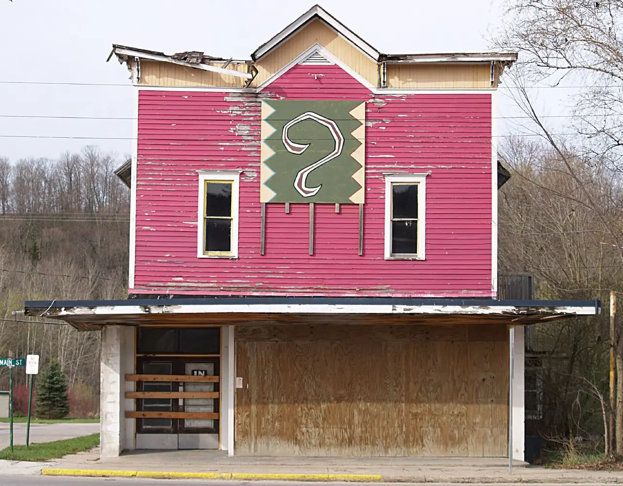 A green question mark on the gable of a pink wooden building