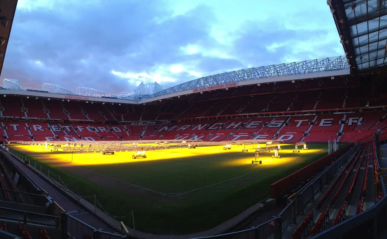 Football stadium at dusk with red seats and a lit pitch
