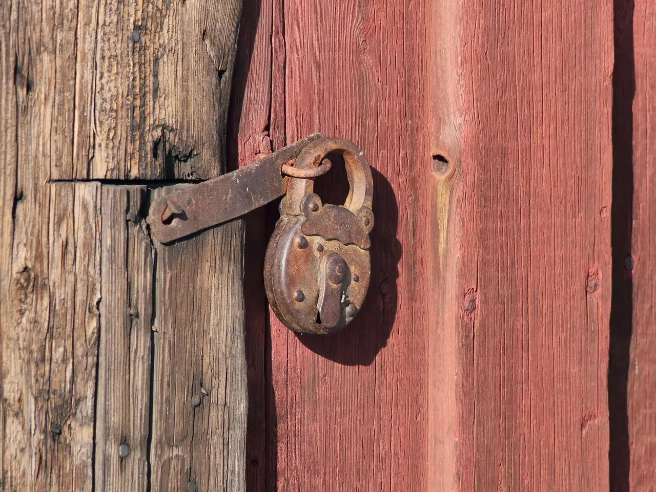 Rusty padlock on a hasp fixed to a red wooden door