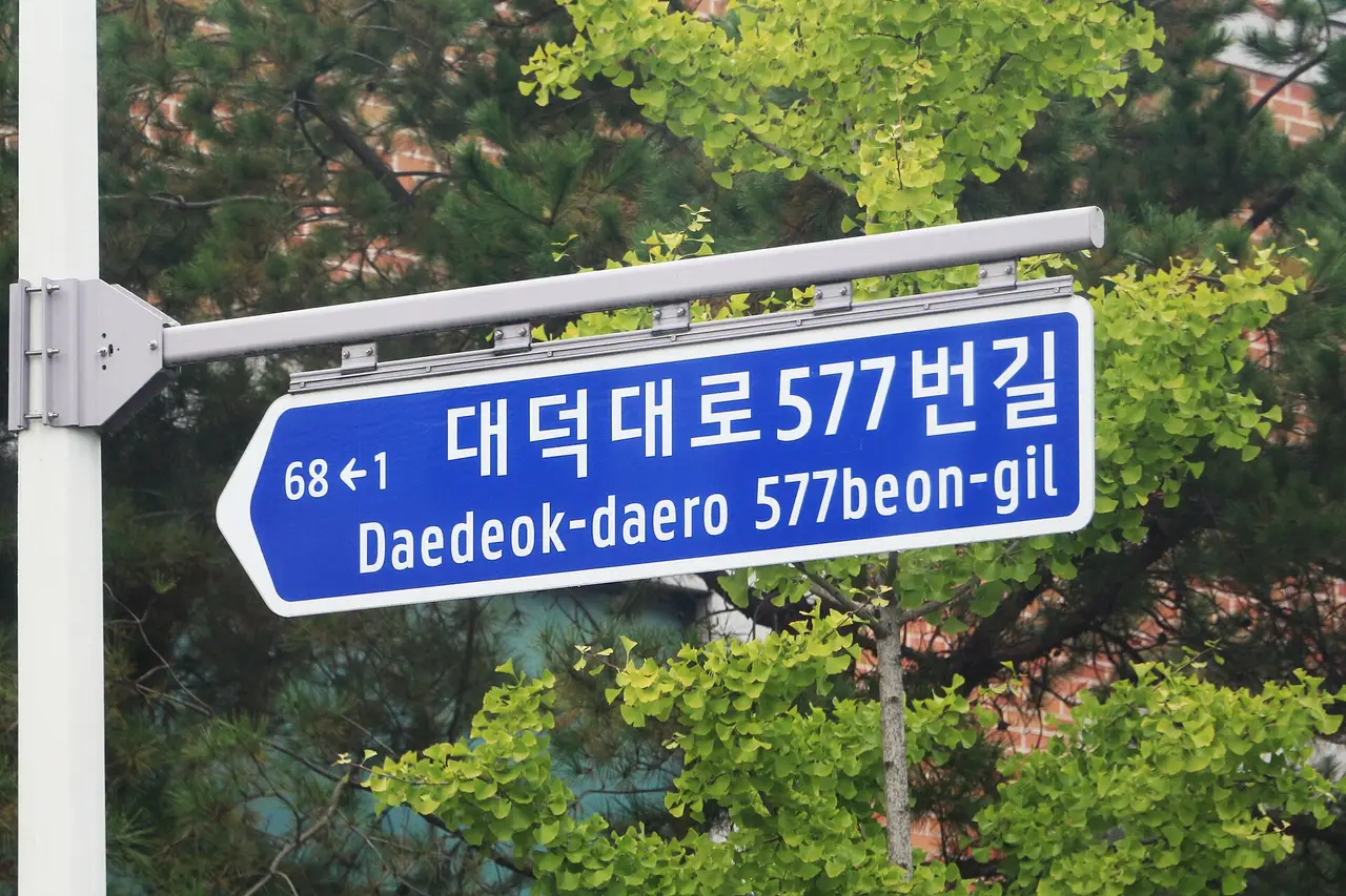 A blue street sign on a pole with Korean and English text