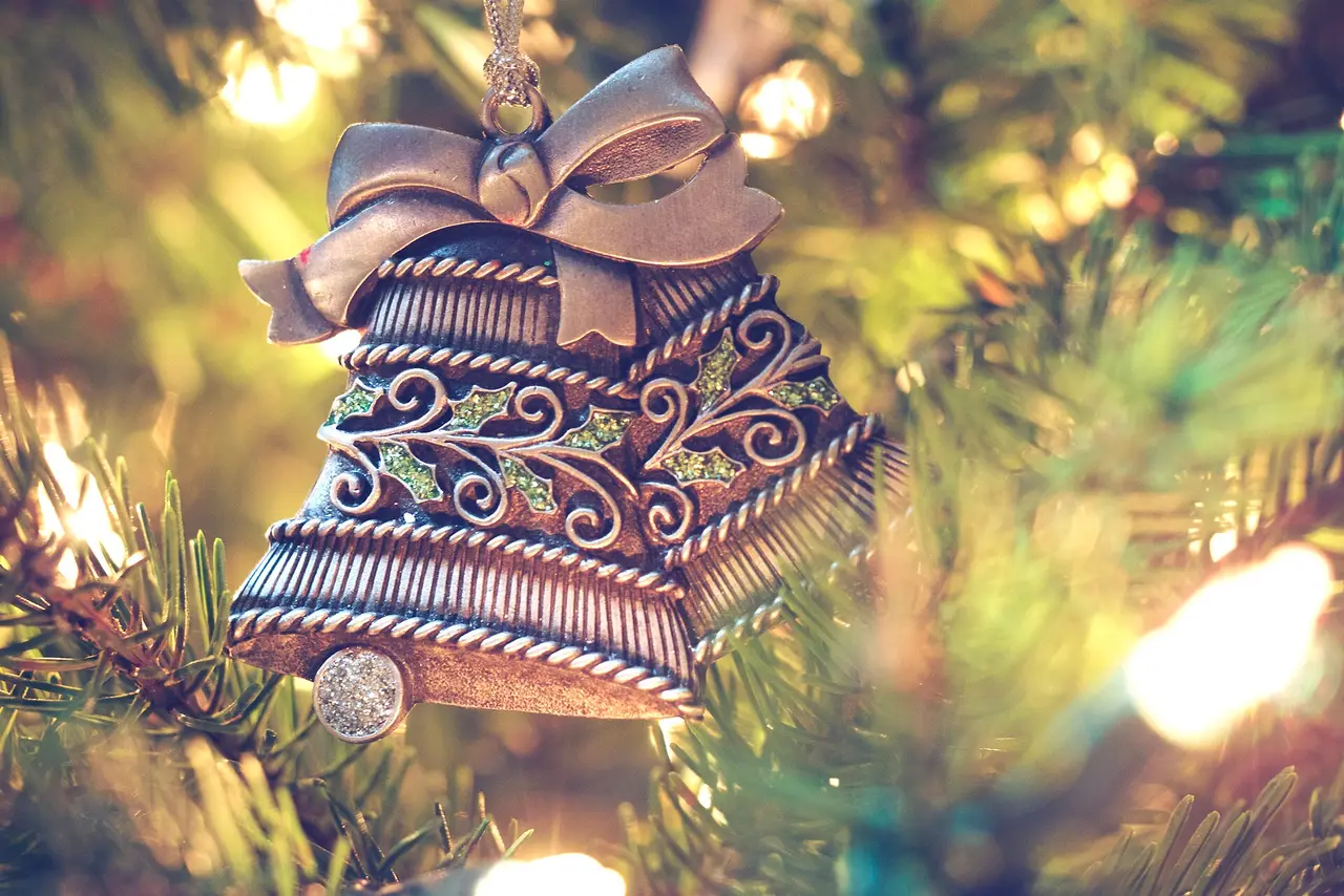 A patterned silver bell ornament with a bow hanging on a lit Christmas tree