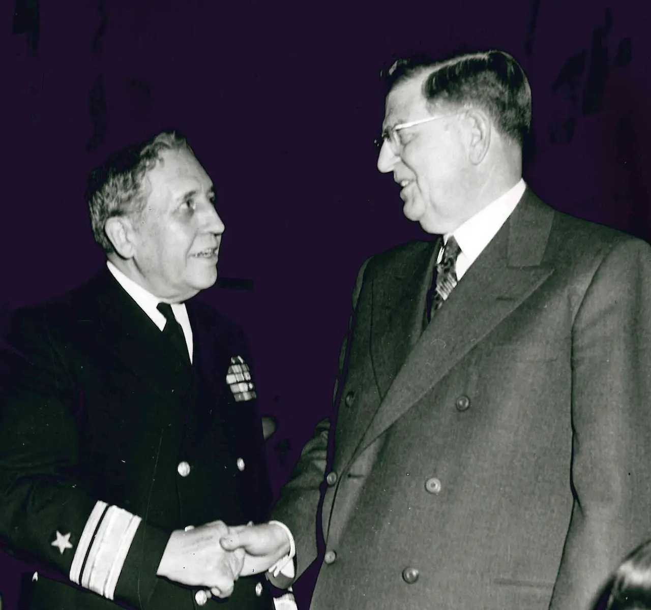 Two men in suit and naval uniform shaking hands in an old photograph