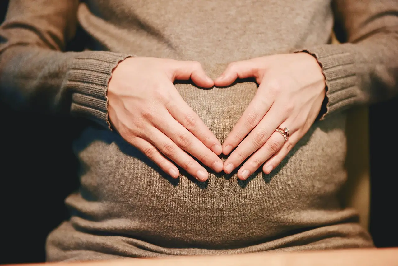 A pregnant woman's hands shaped into a heart on her belly