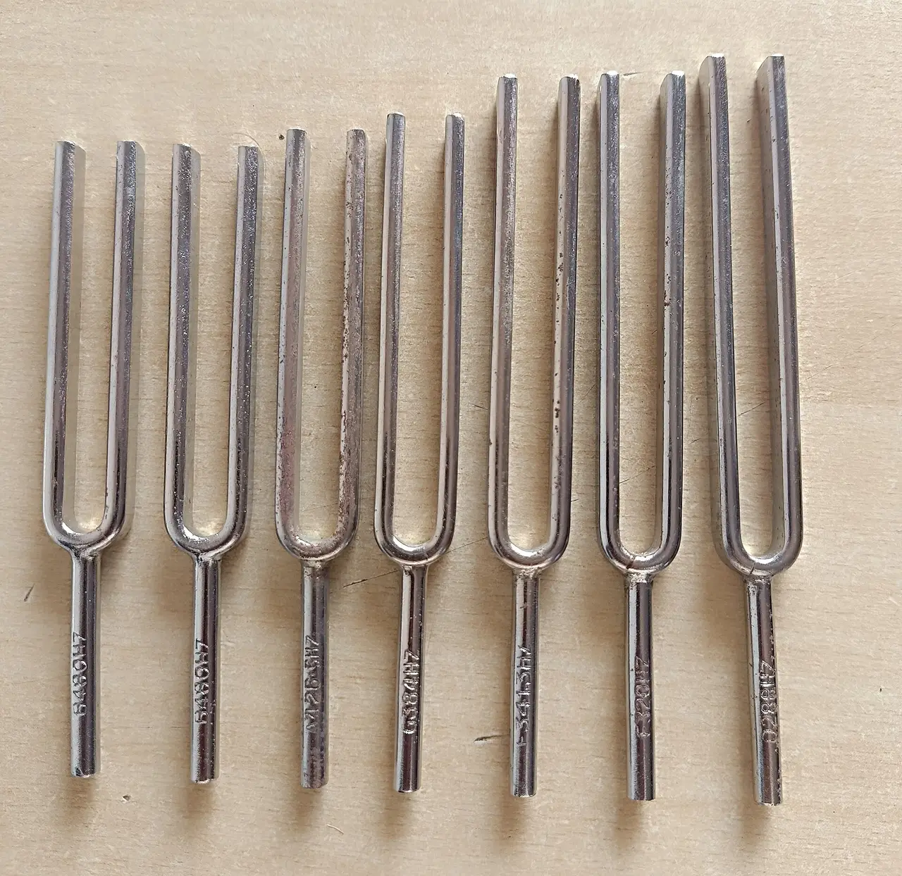 A row of steel tuning forks of different sizes on a wooden surface