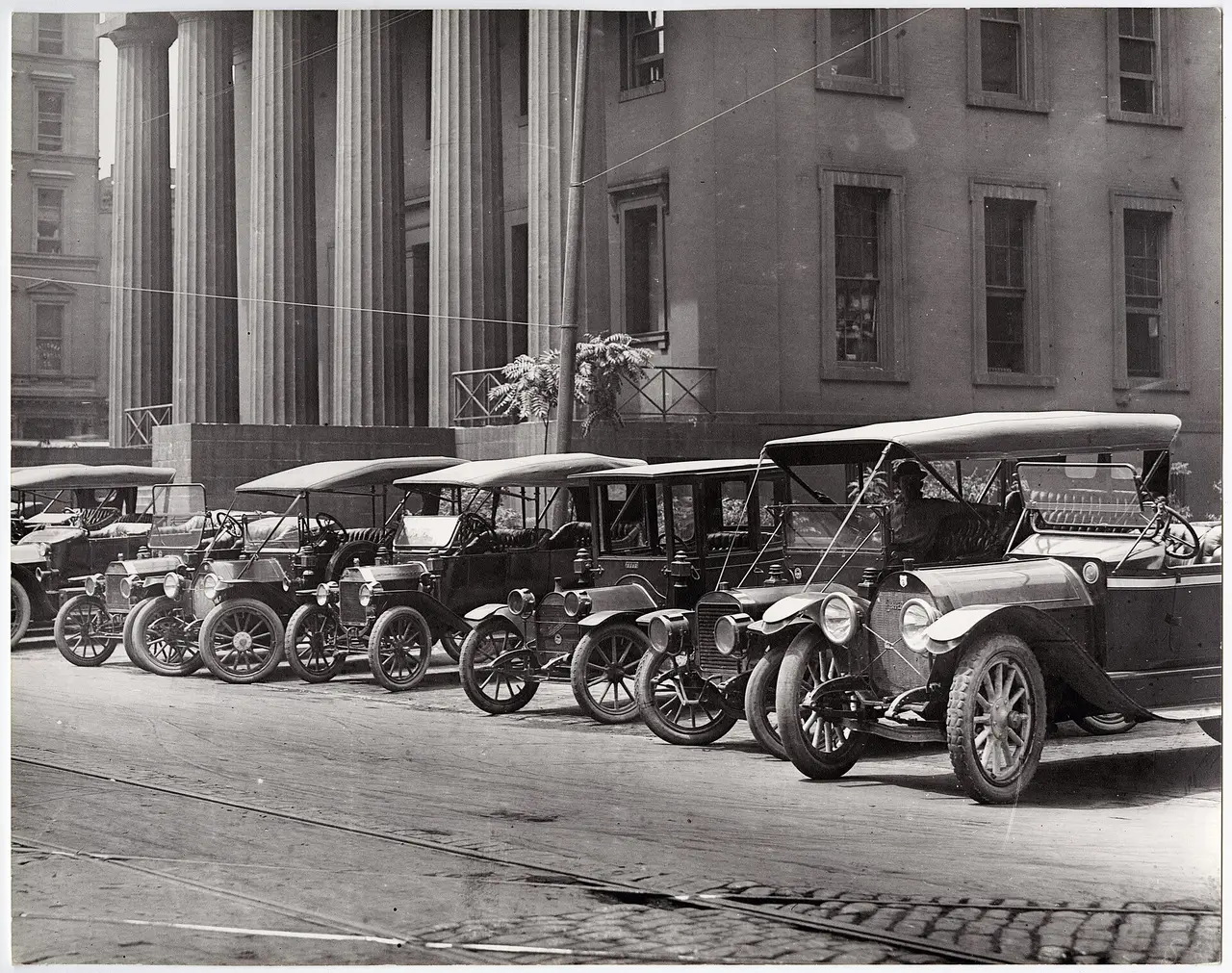 Early motor cars parked in a row outside a columned building