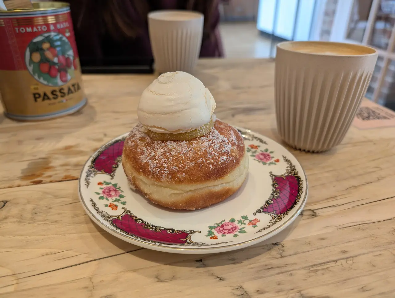 A cream-topped doughnut on a floral plate beside a coffee cup
