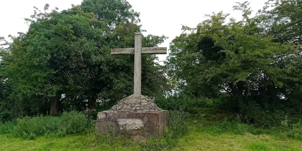 A stone cross on a stone base among green trees