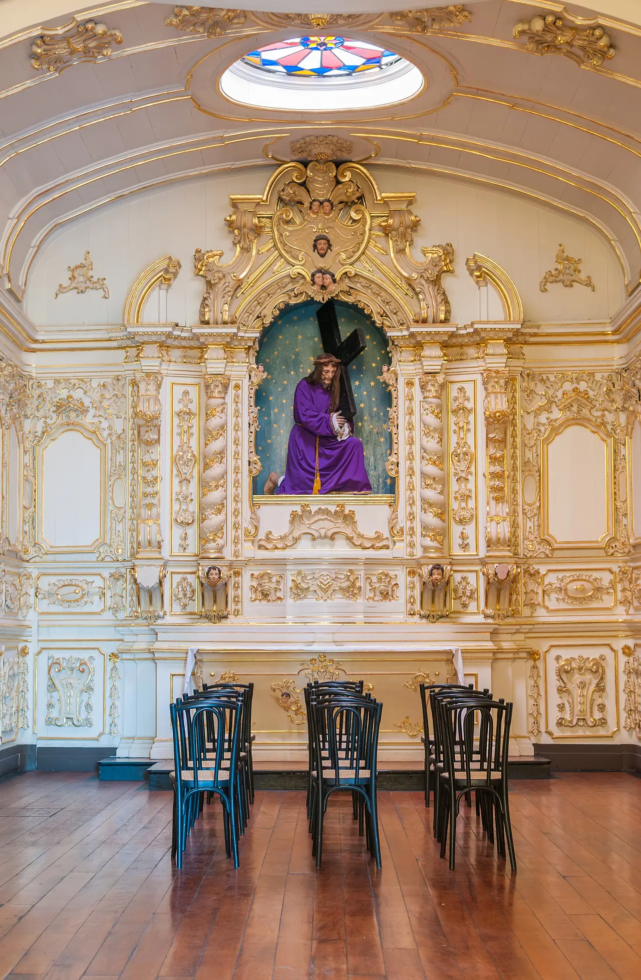 A gilded church altar with a purple-robed statue and chairs before it
