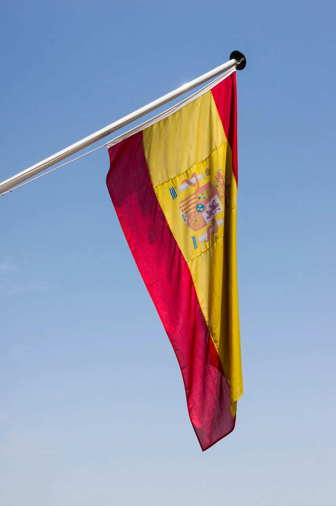 A red and yellow Spanish flag on a pole against a blue sky