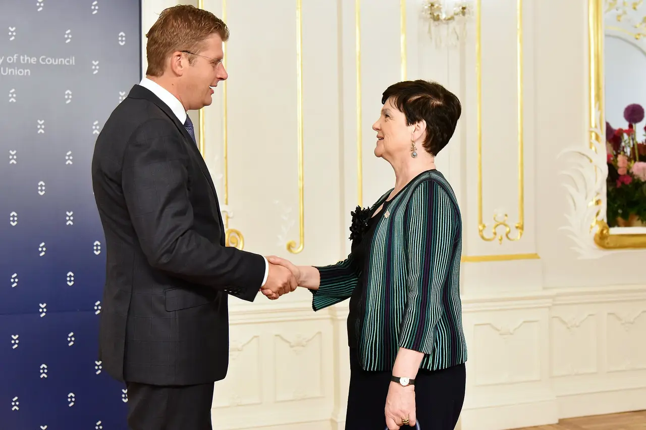 A man and a woman shaking hands in front of a blue EU presidency backdrop
