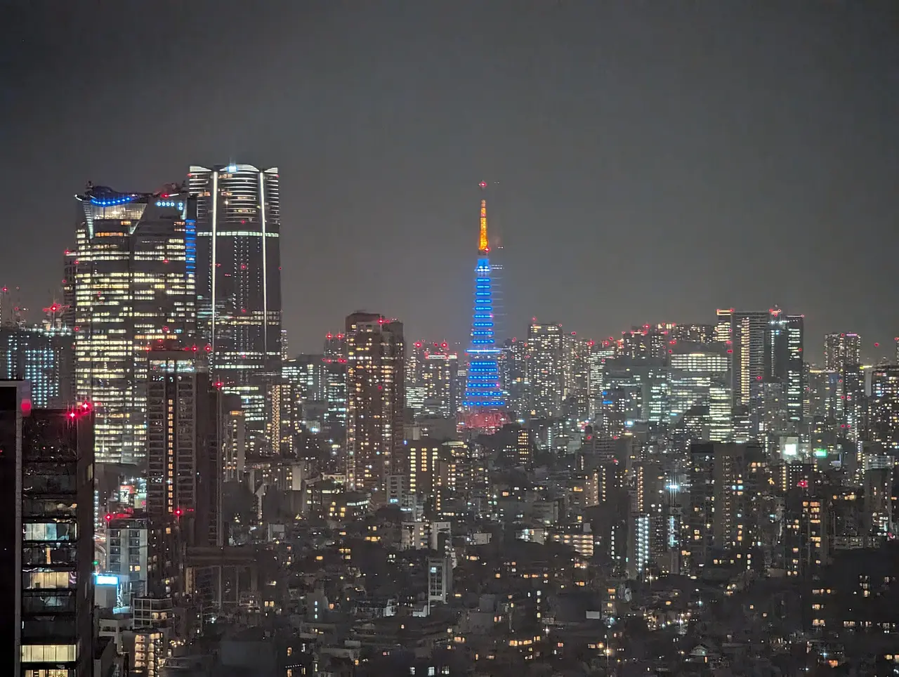 Tokyo Tower glowing blue at night among city skyscrapers