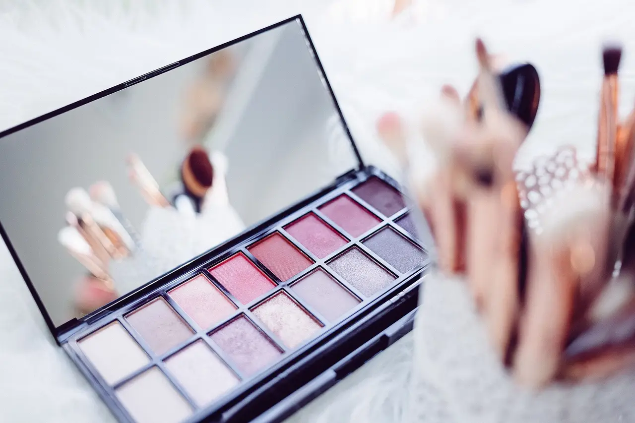 An open eyeshadow palette with a mirror beside pink make-up brushes
