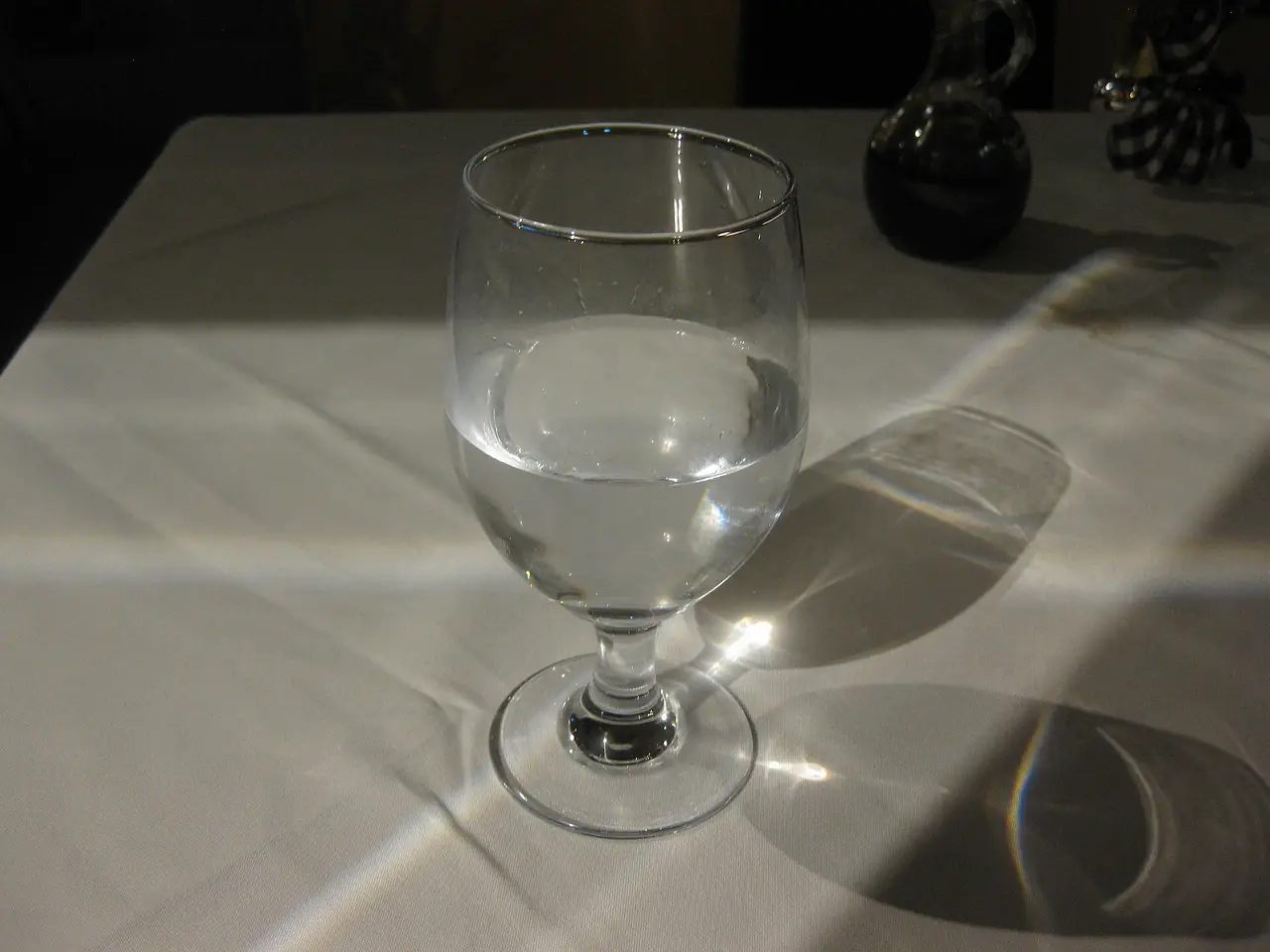 A stemmed glass of water on a tablecloth catching the light