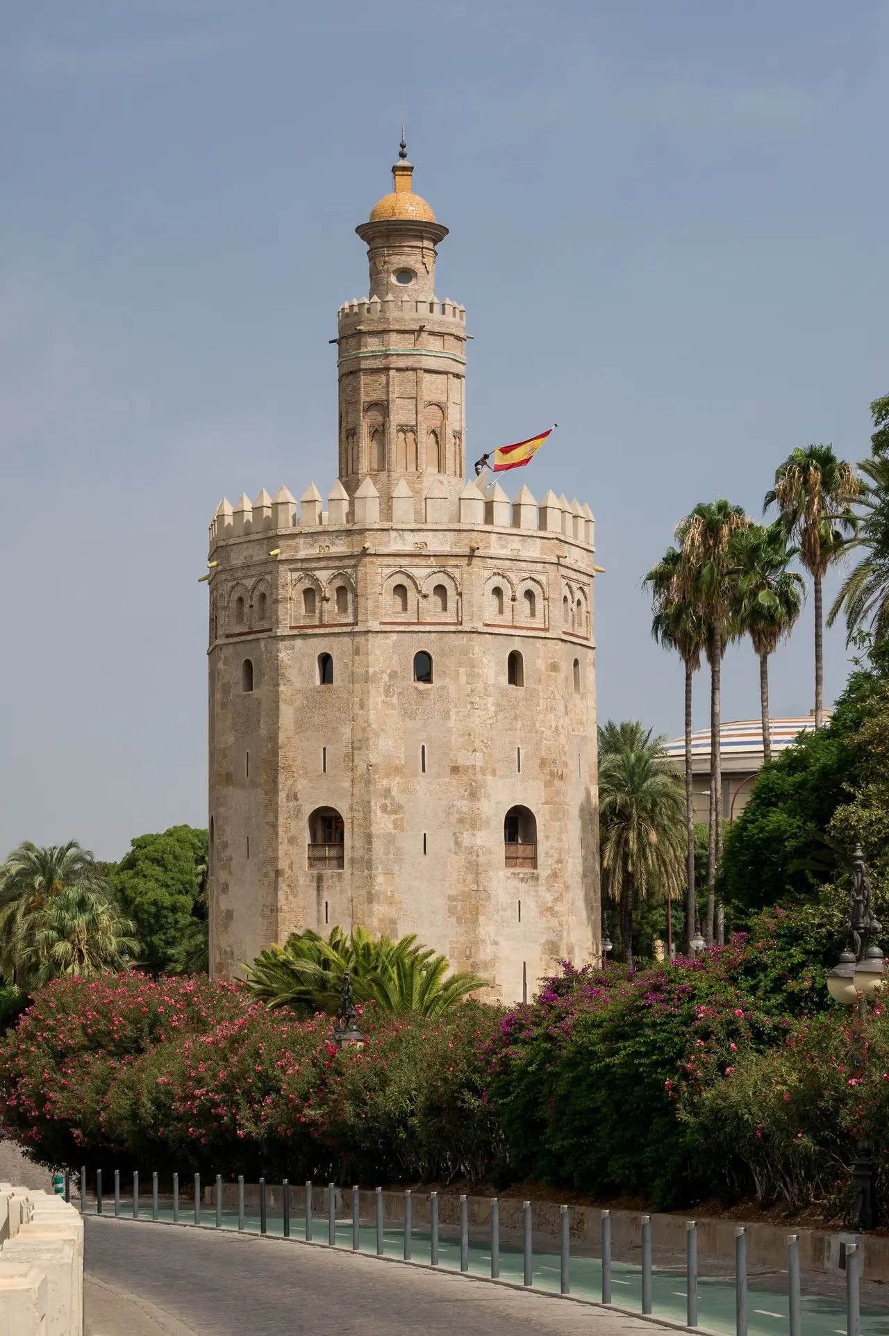 A tall stone tower with a small Spanish flag beside palm trees