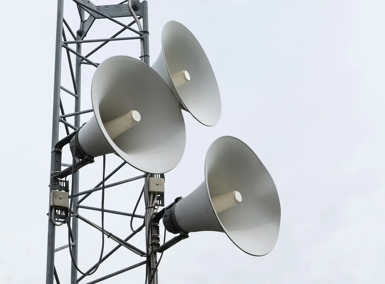 Three white horn loudspeakers on a steel mast under a grey sky