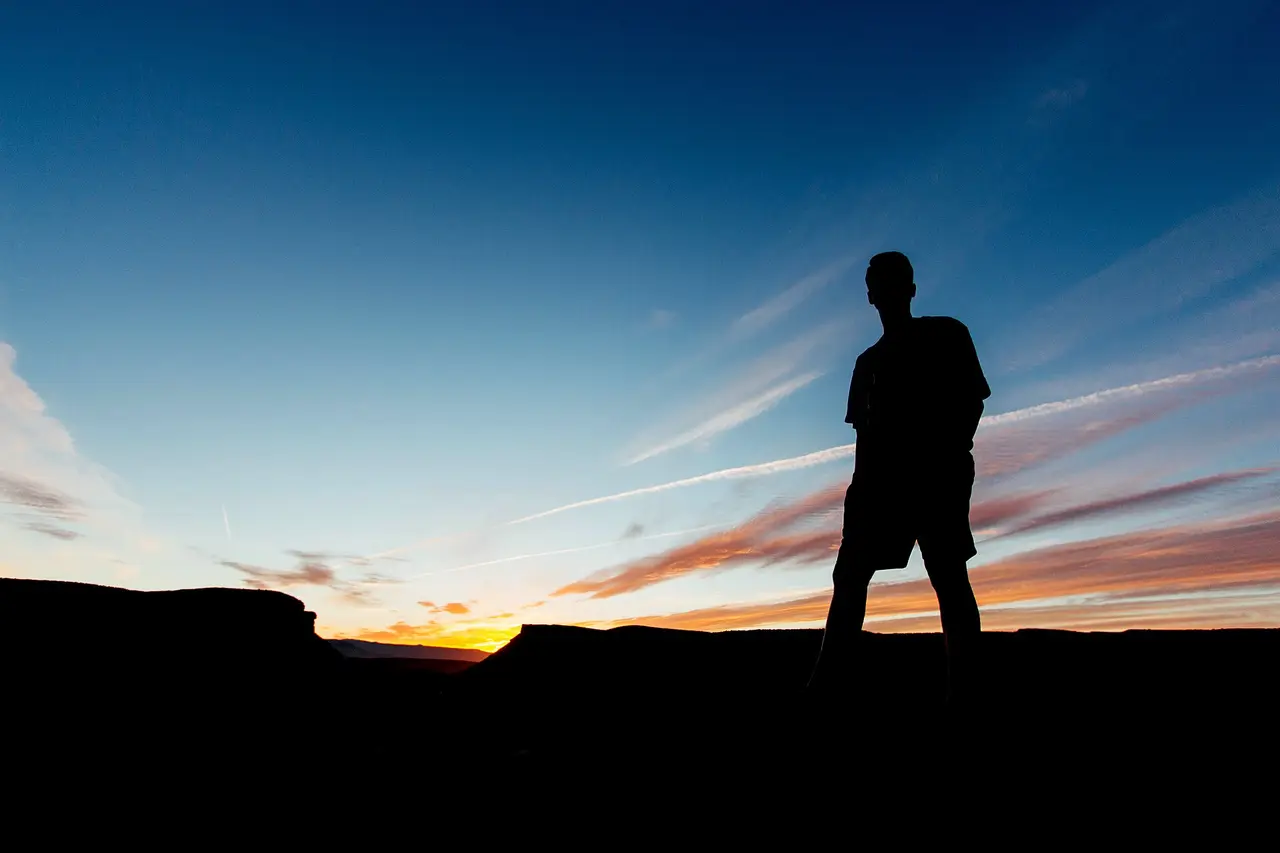 Dark silhouette of a man on a ridge under a sunset sky
