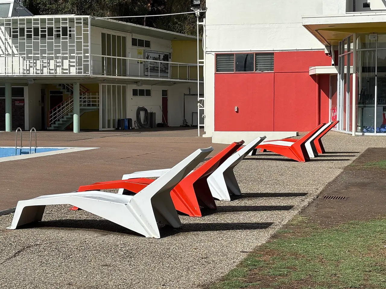 Red and white sun loungers on paving beside a swimming pool