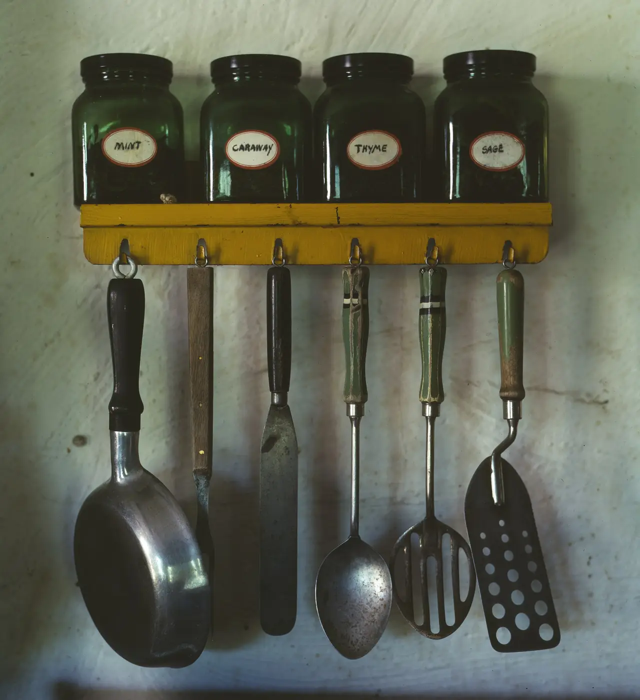 Kitchen utensils hanging below a rack of herbs and spices