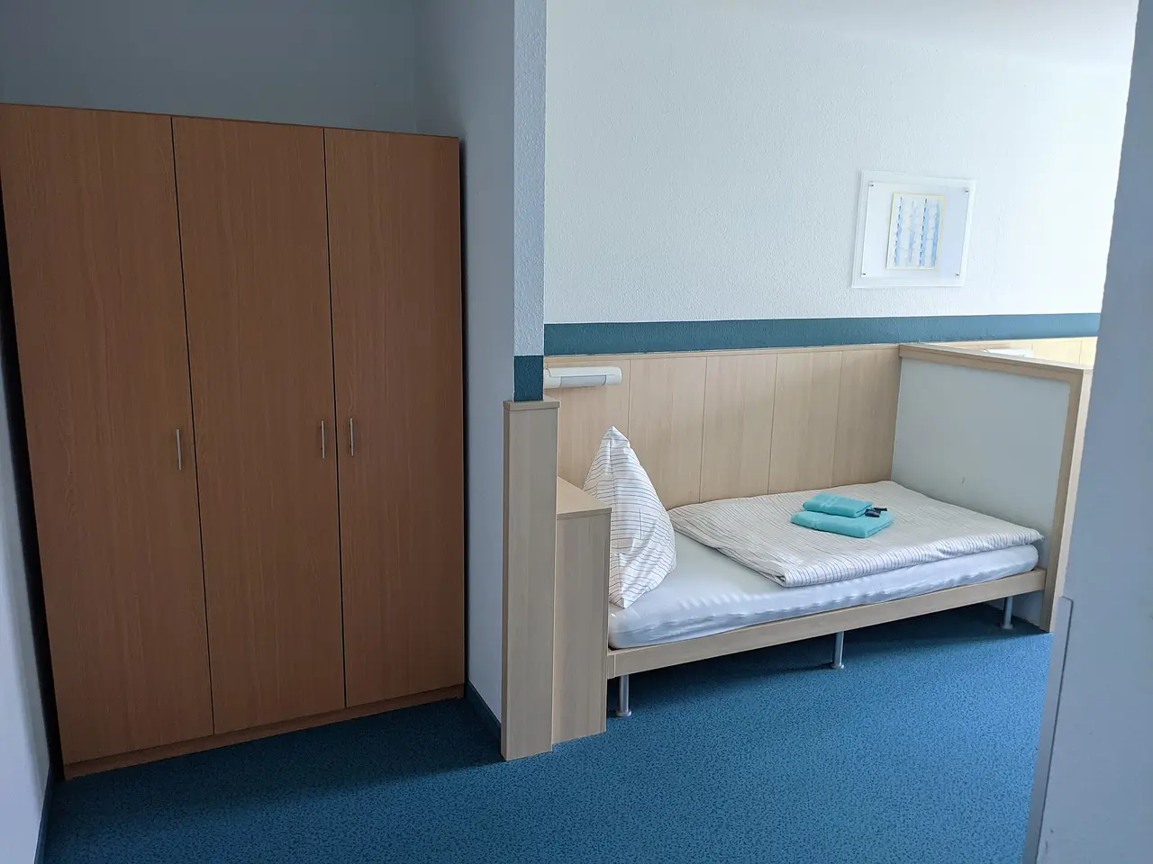A tall wooden wardrobe beside a single bed in a plain hostel room