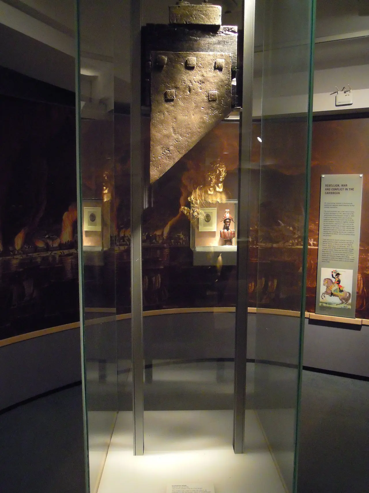 A tall wooden guillotine inside a glass museum case