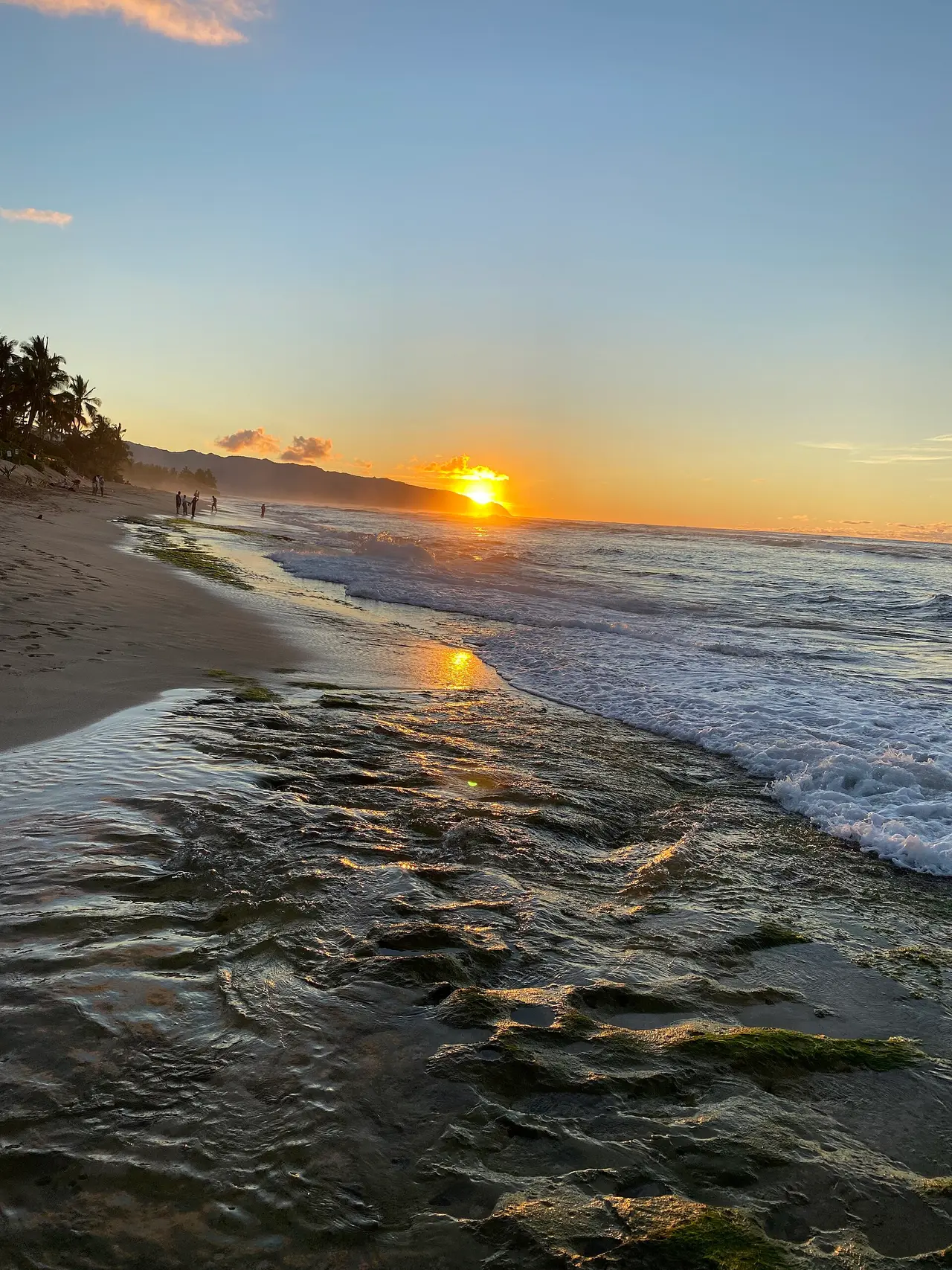 The sun setting over a Hawaiian beach with waves on wet sand