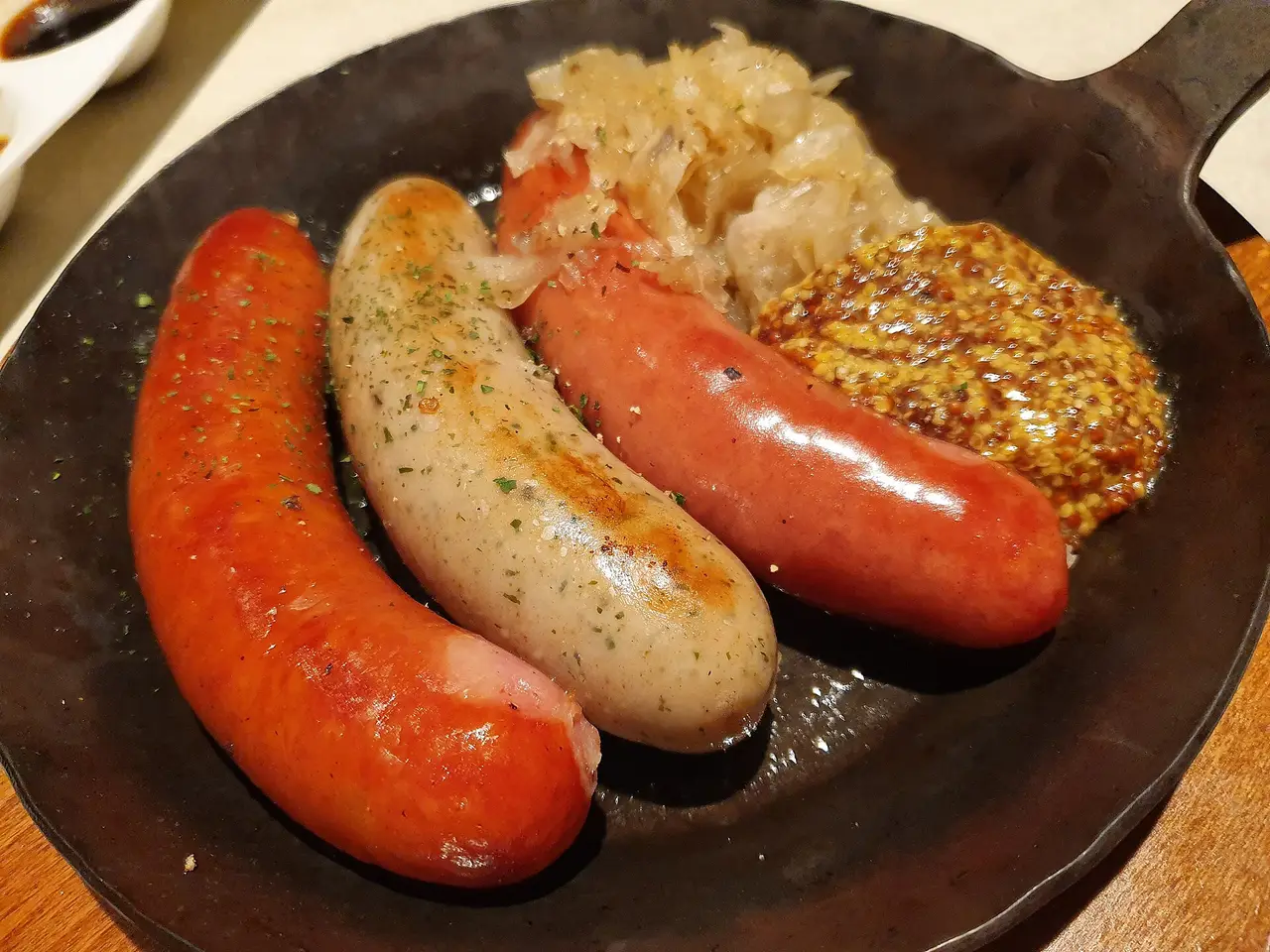 Three sausages in a black pan with sauerkraut and mustard