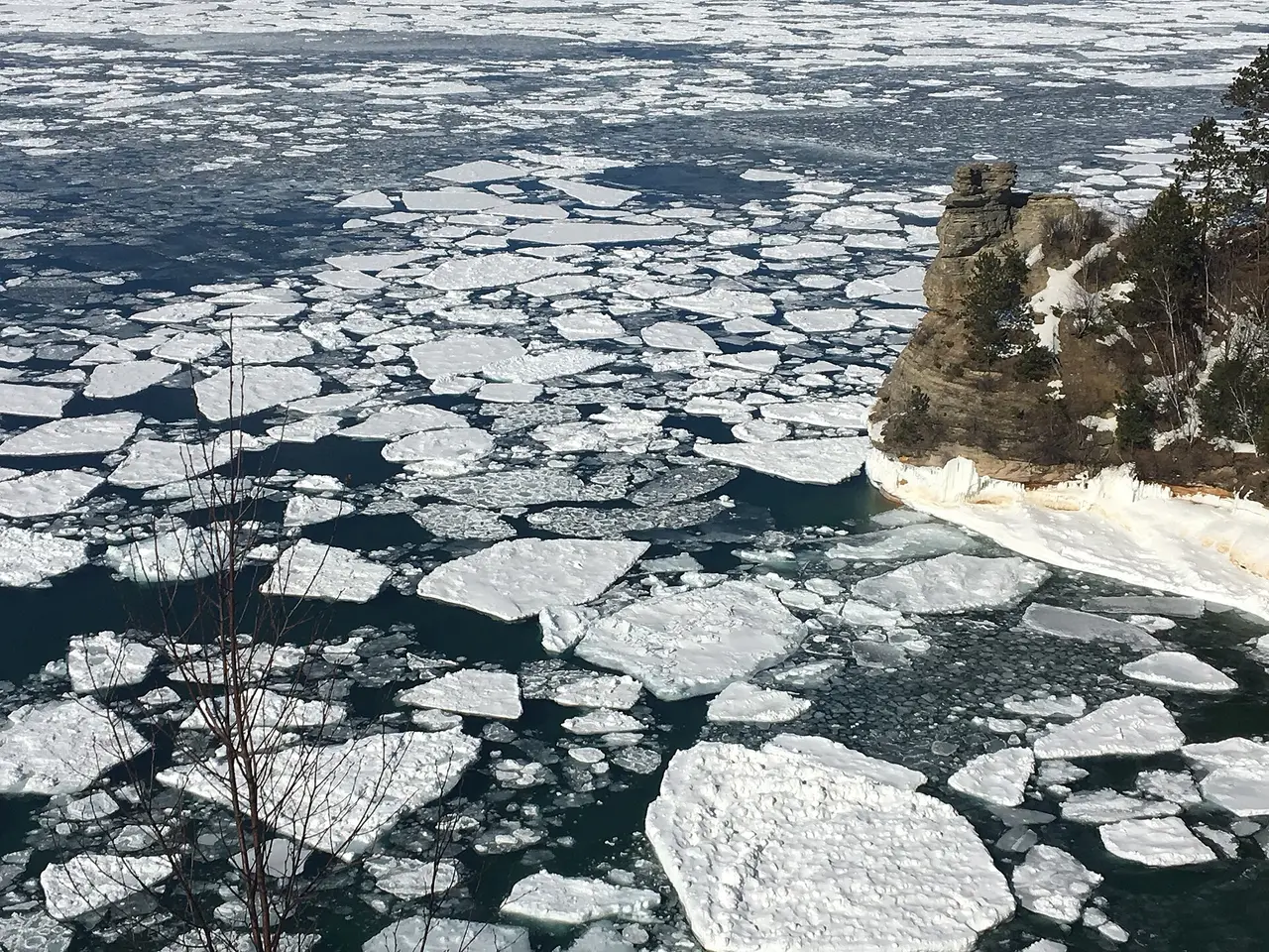 Broken ice floes on dark water beside a rocky cliff