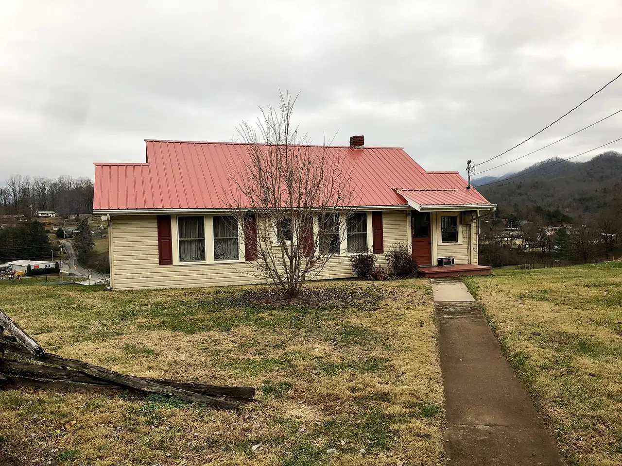 A cream house with a red roof on a grassy lot, with hills behind