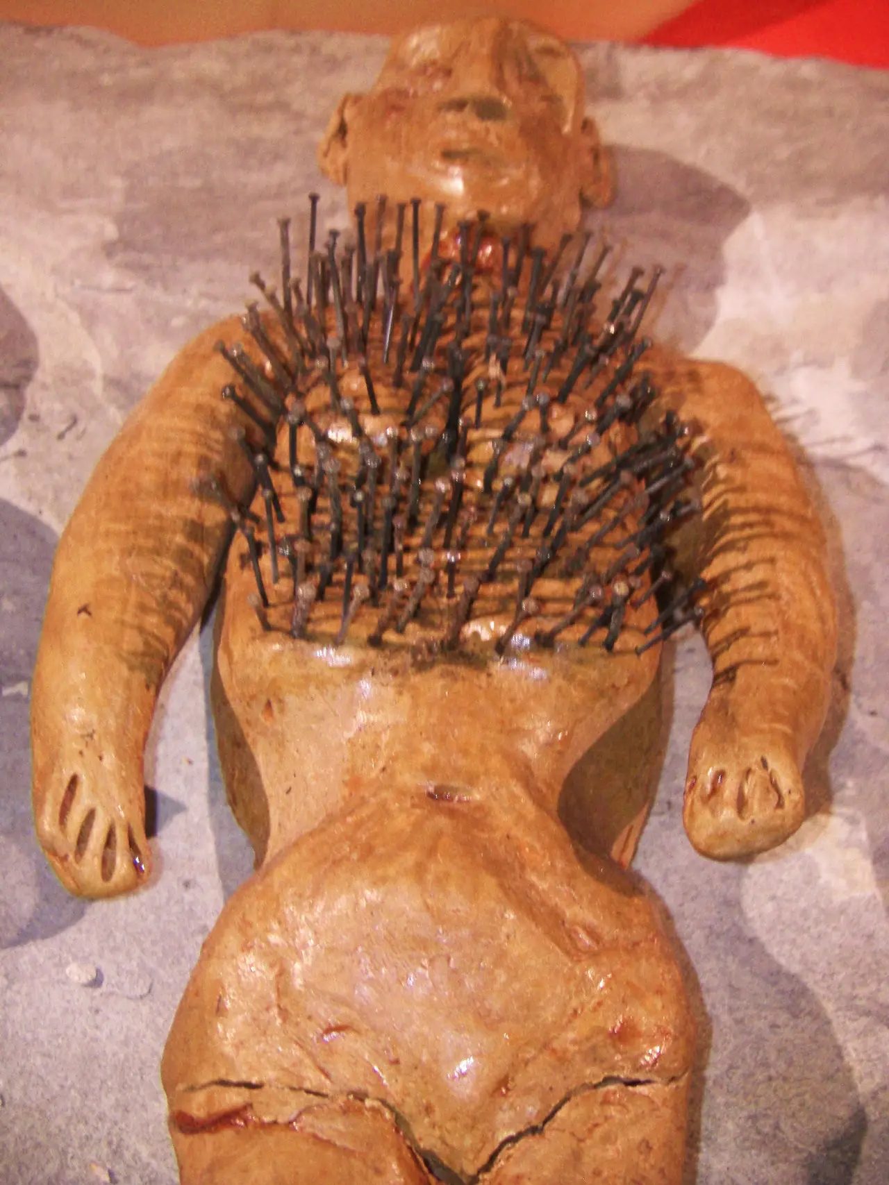A clay figure of a person with dozens of pins stuck in its chest