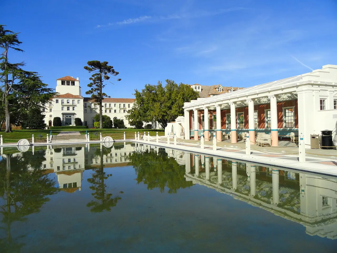 A long still pool beside a white colonnade under a blue sky