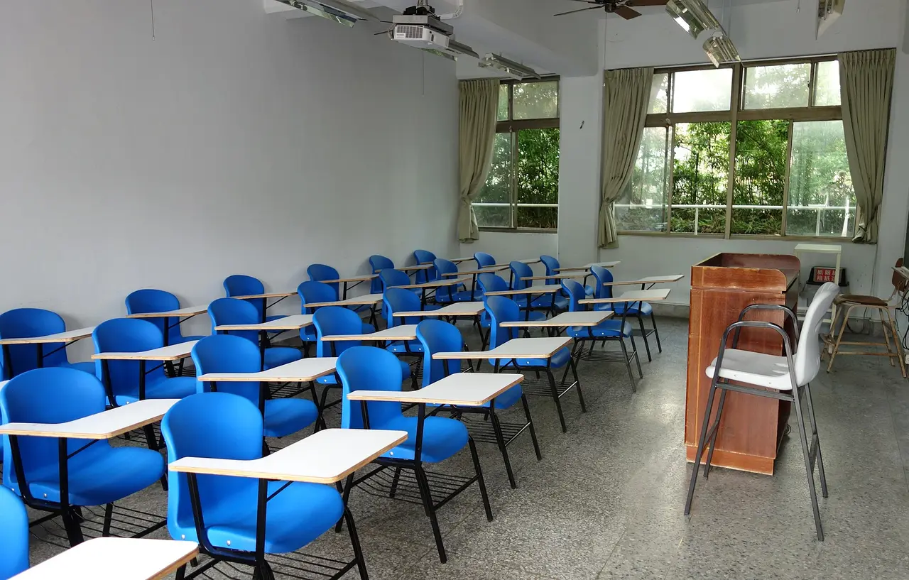 Rows of blue chairs with desks facing a lectern in an empty classroom