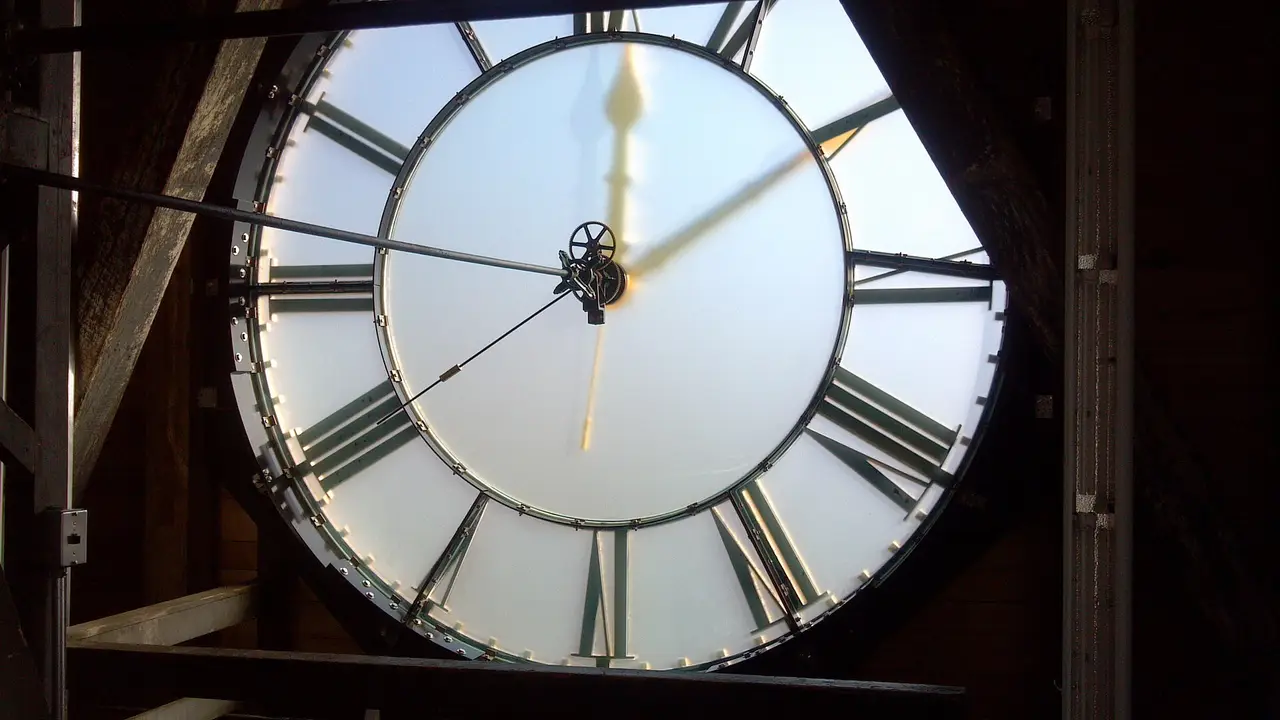 A backlit clock face with Roman numerals seen from behind