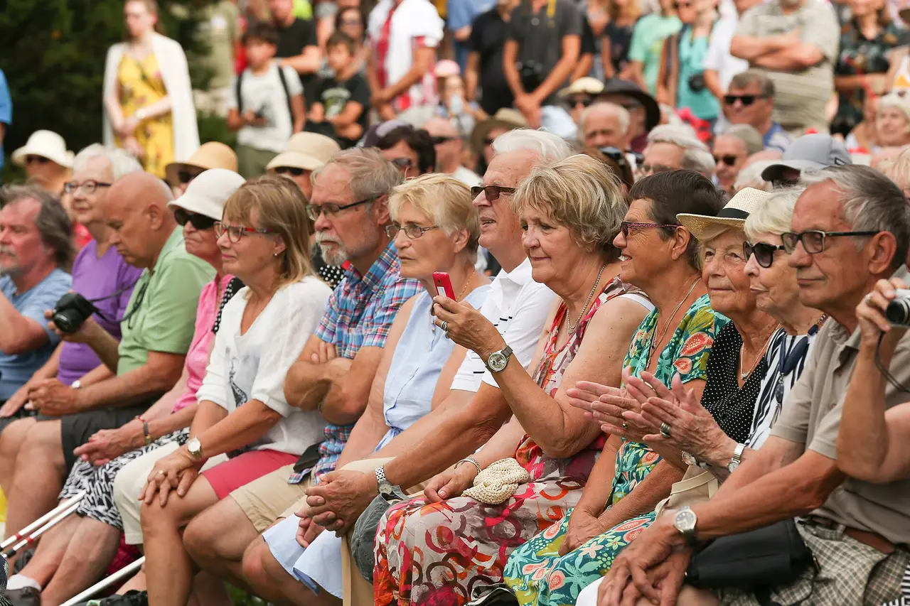A seated crowd of adults in summer clothes watching a performance outdoors