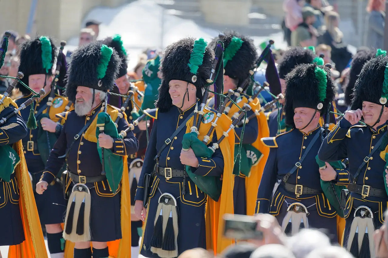 A row of pipers in feather bonnets marching along a street
