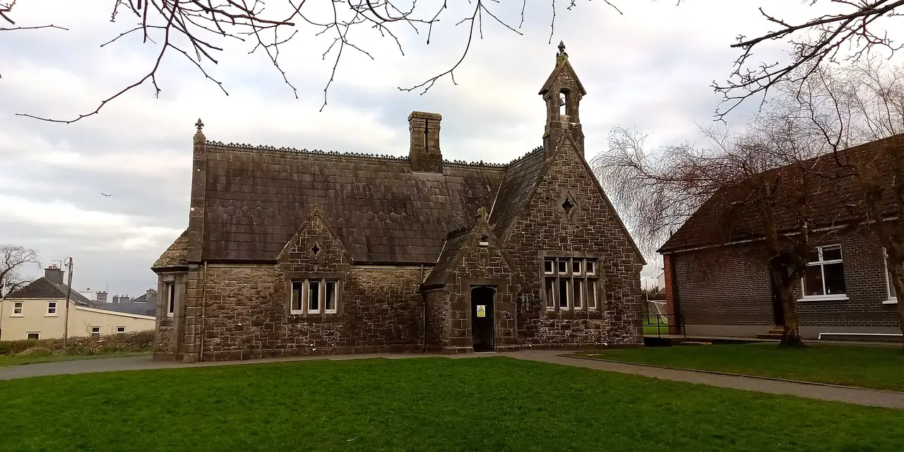A stone school house with a bell turret on a lawn