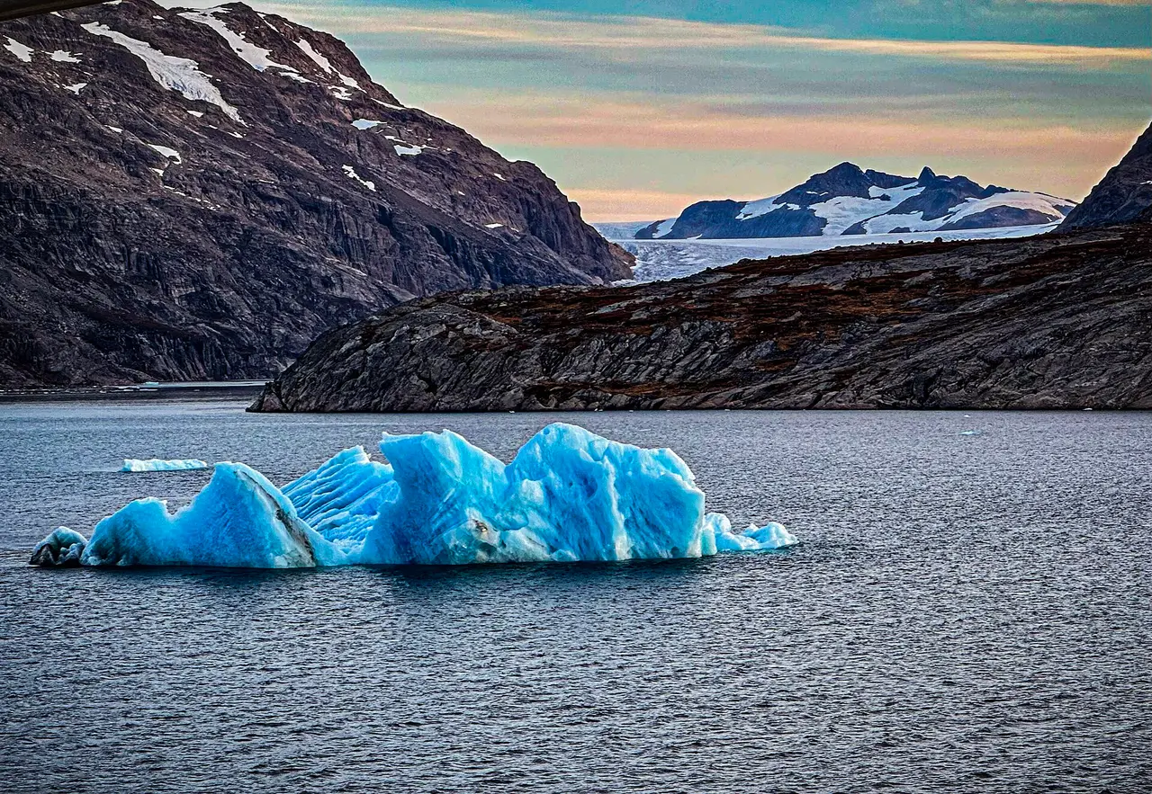 A blue iceberg on dark water in front of mountains