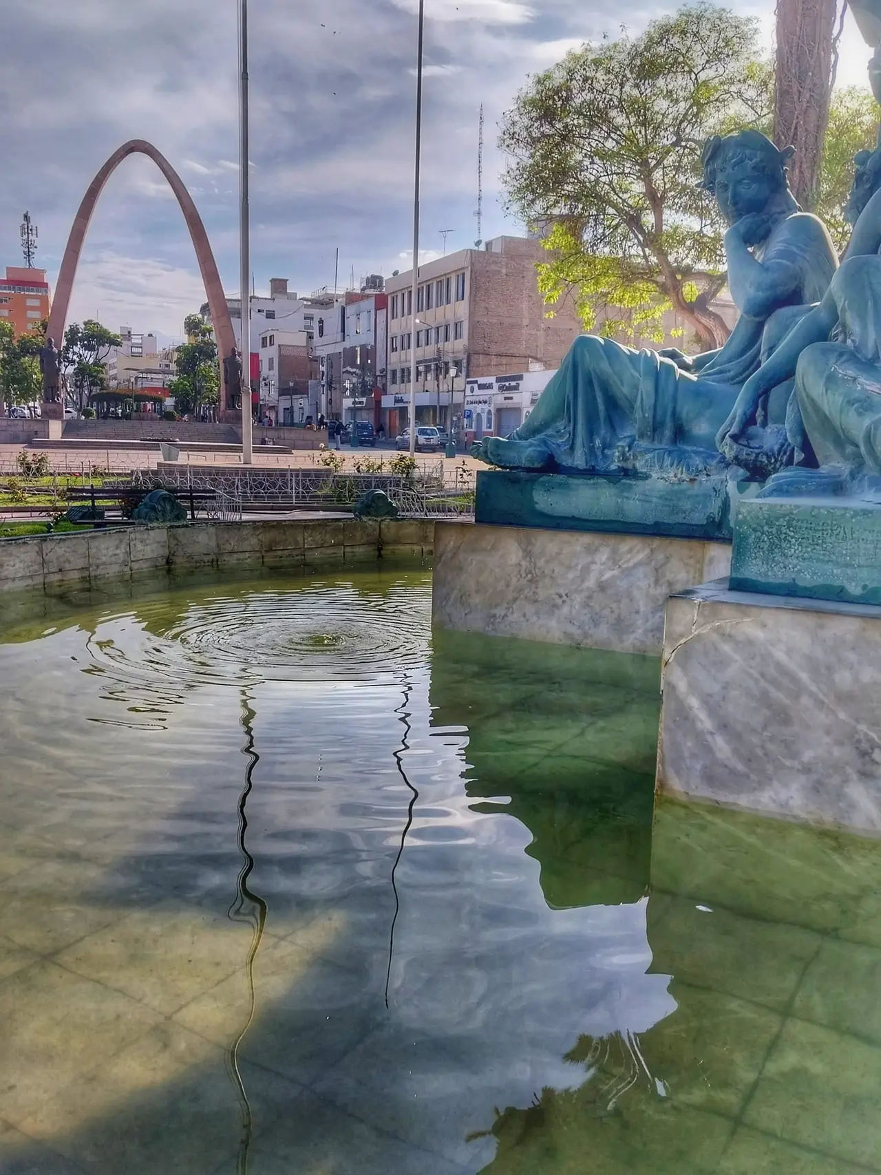 A tall red parabolic arch beside a fountain and statue