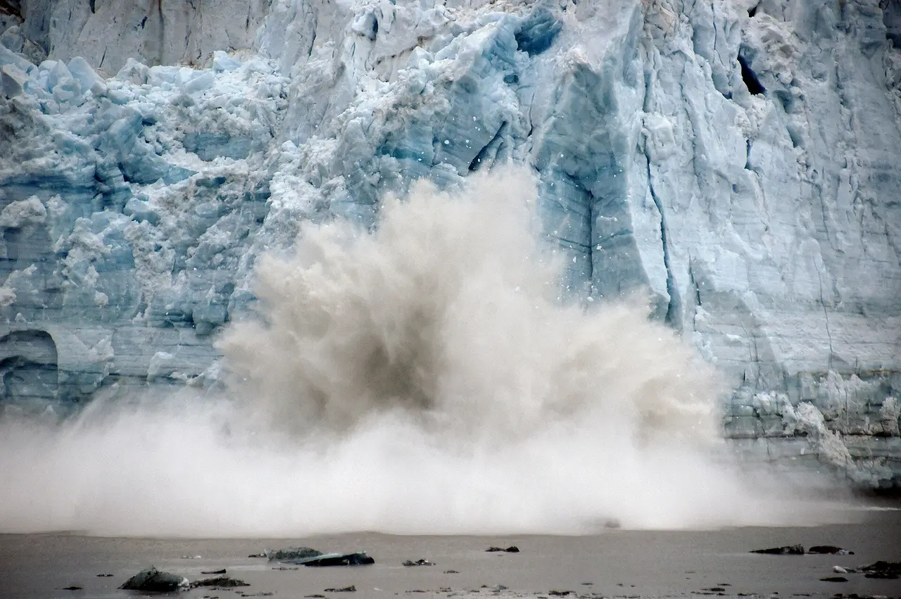 Blue glacier ice face with spray as a piece falls into the water