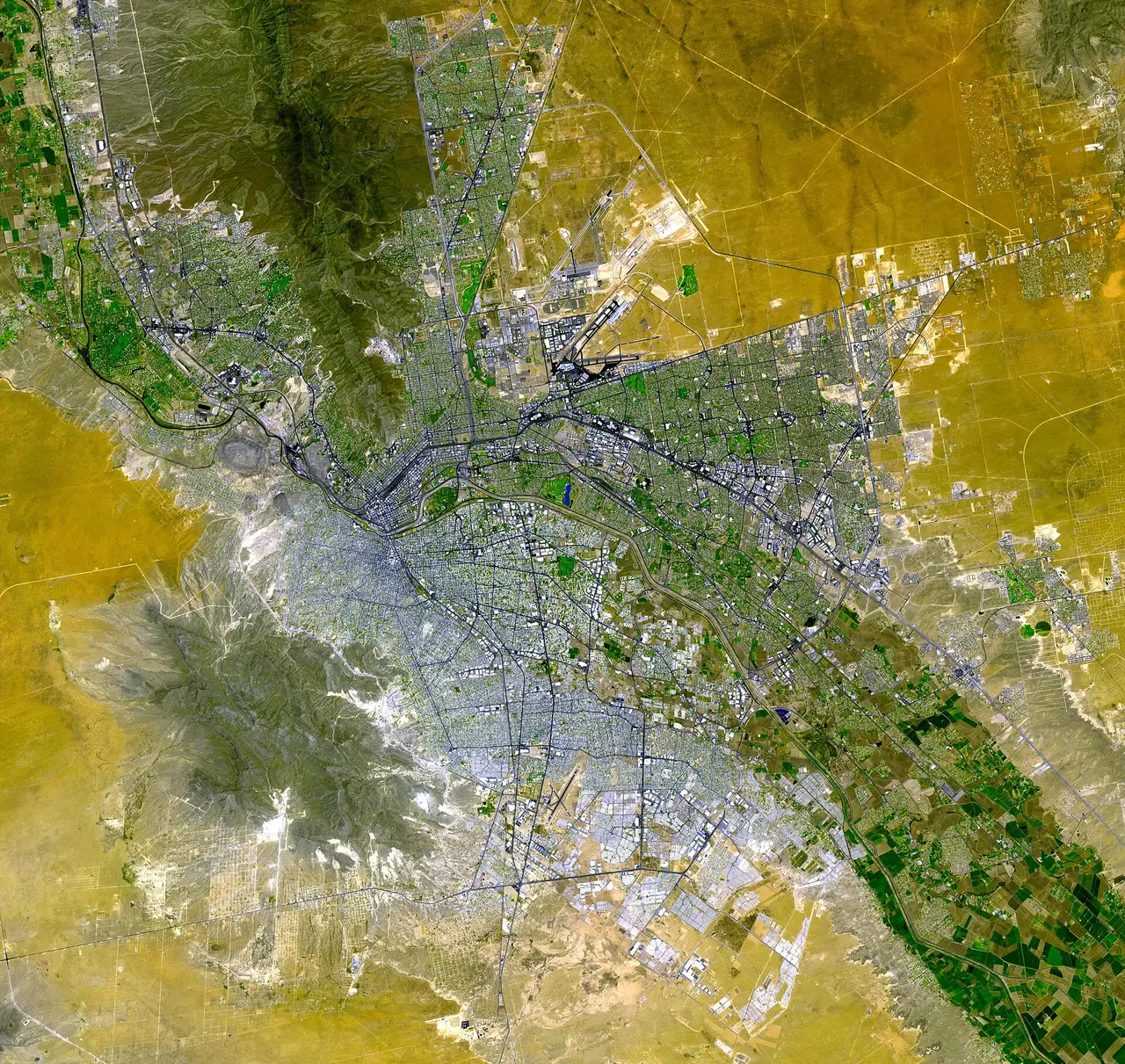 A satellite view of two cities spread across a yellow-green desert plain
