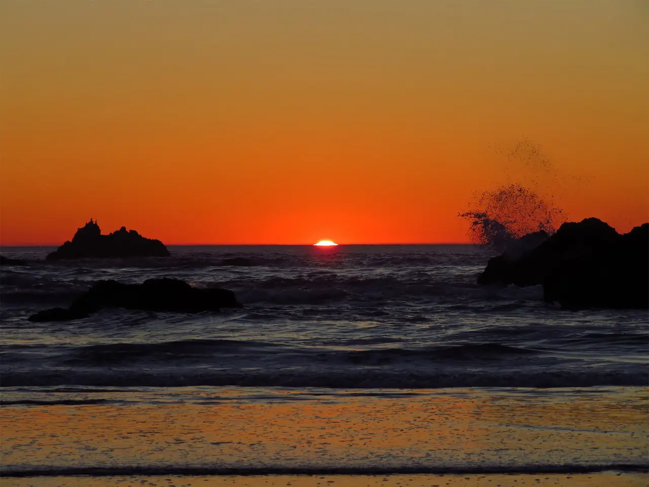 An orange sky over the sea with dark rocks in the surf