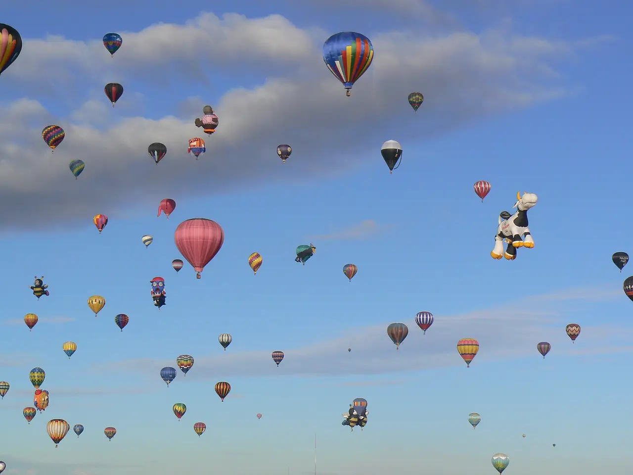 Many hot air balloons floating in a blue sky with clouds
