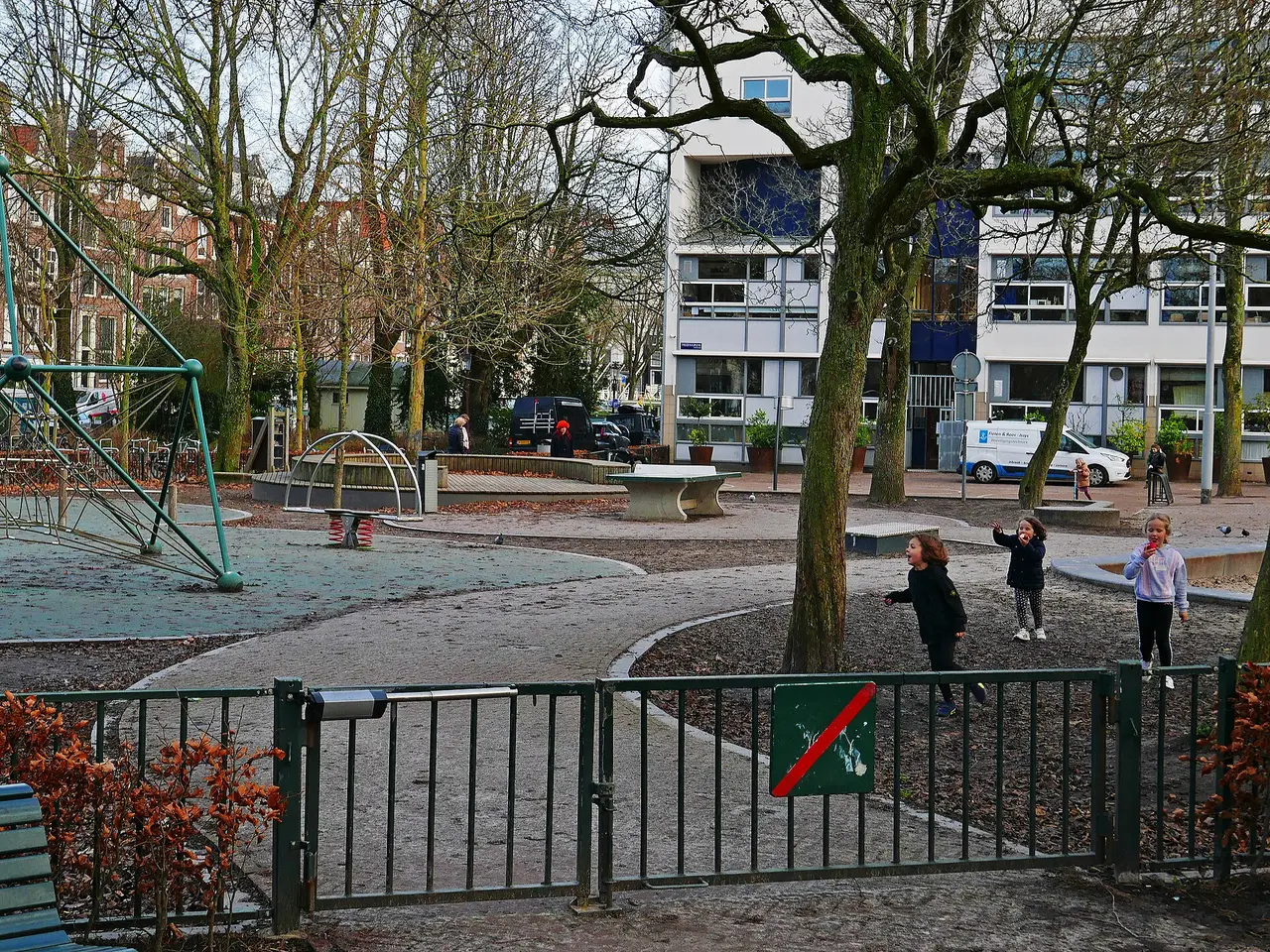 Children at play in a city playground beside bare winter trees